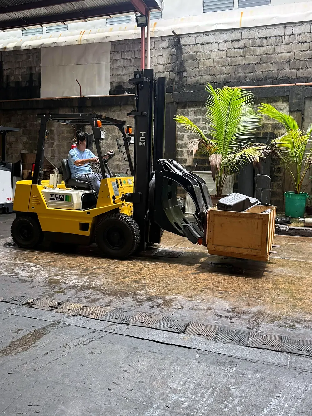 TCM FG25 forklift with a rotating clamp attachment carrying a wooden crate